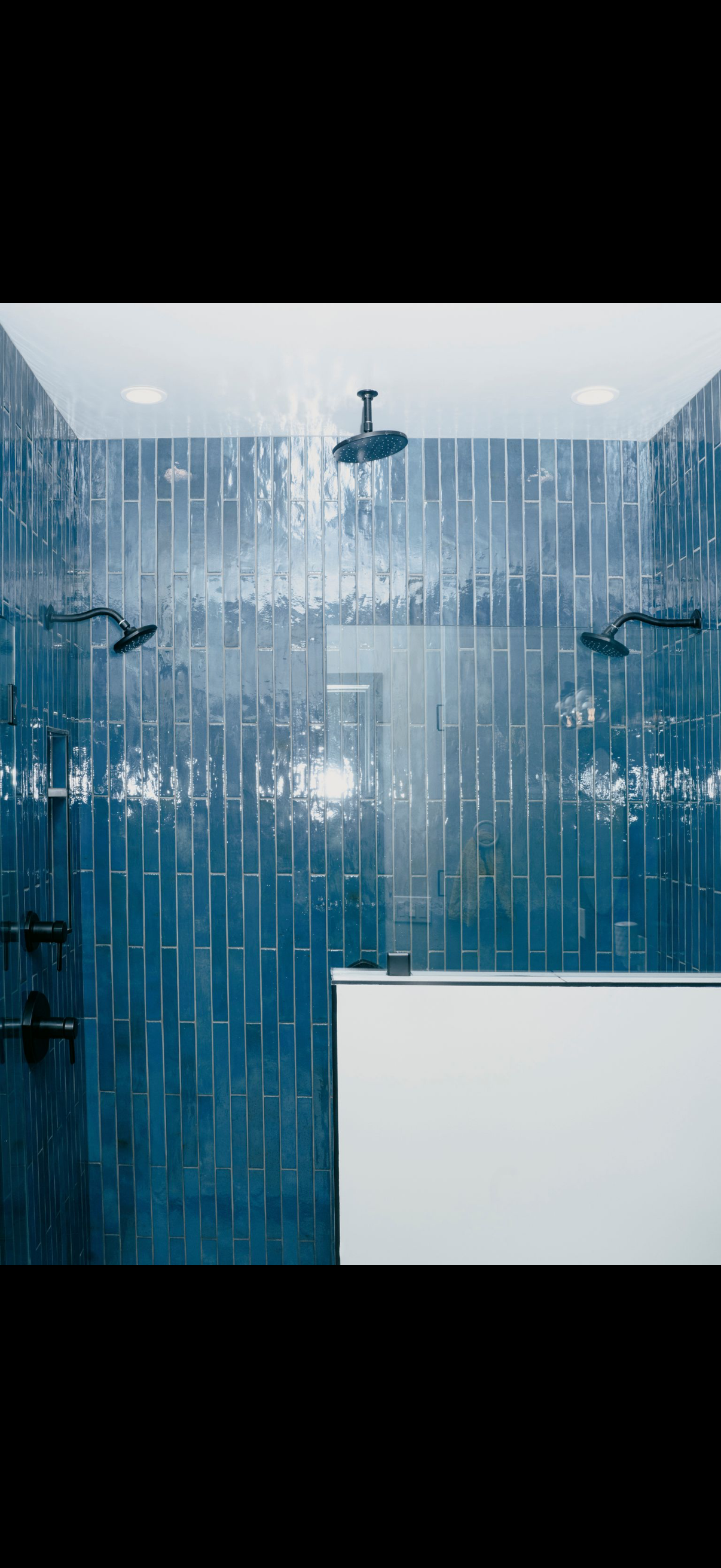 Blue-tiled shower with multiple showerheads, black fixtures, and a white shelf.