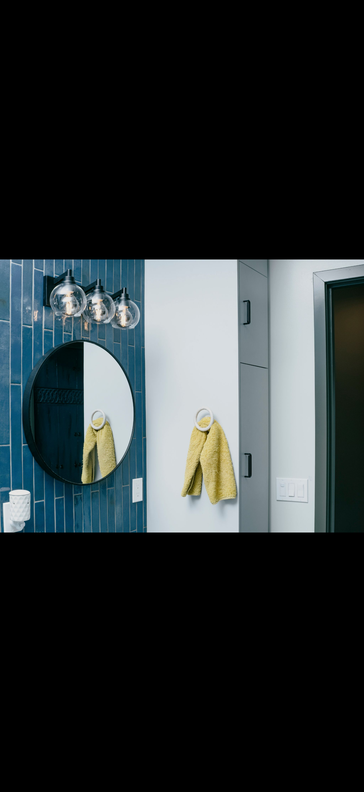 Bathroom with blue tile, round mirror, yellow jacket, and silver lights.