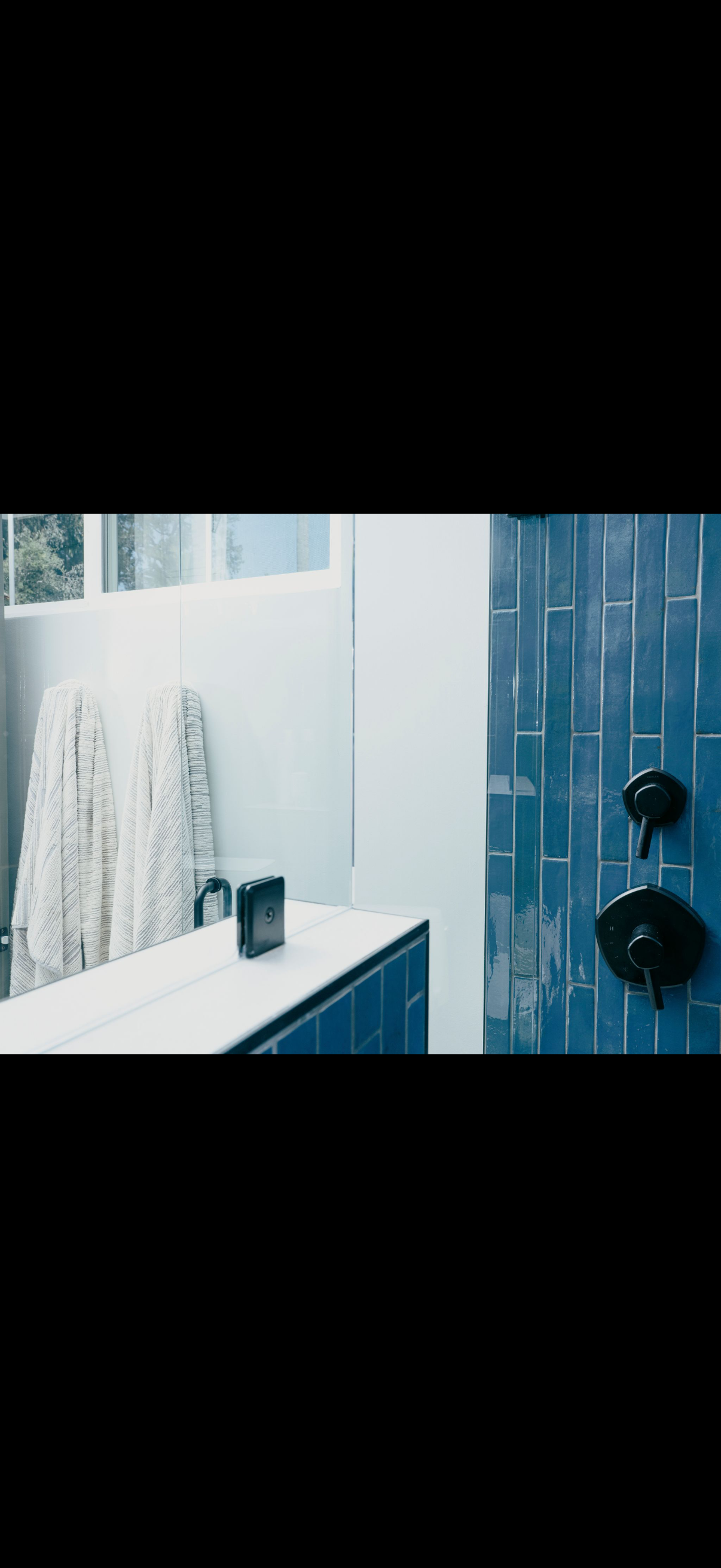 Bathroom interior with blue tiled shower, black fixtures, white wall, and a white towel.