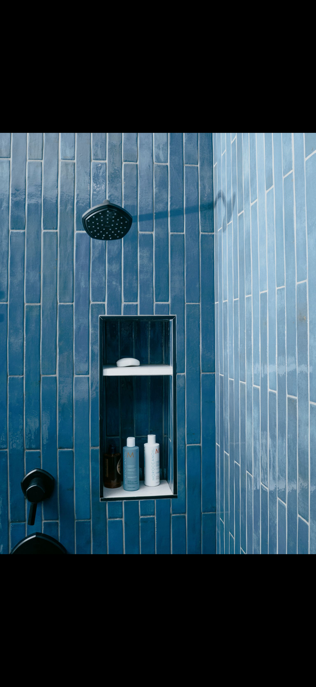 Blue-tiled shower with a built-in shelf holding soap and bottles, and a black shower head and faucet.