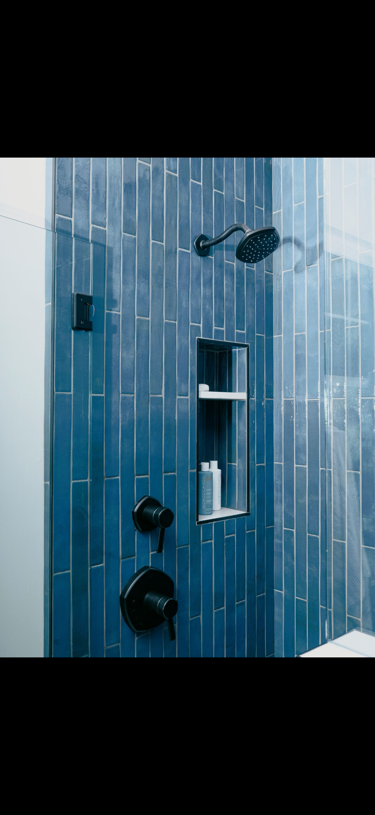 Blue tiled shower with black fixtures and a built-in shelf.