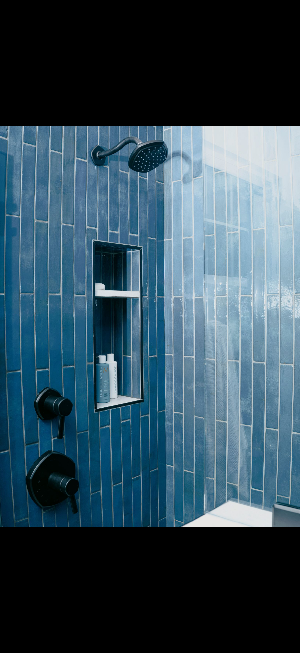 A blue tiled shower with black fixtures. A shampoo niche is built into the wall.