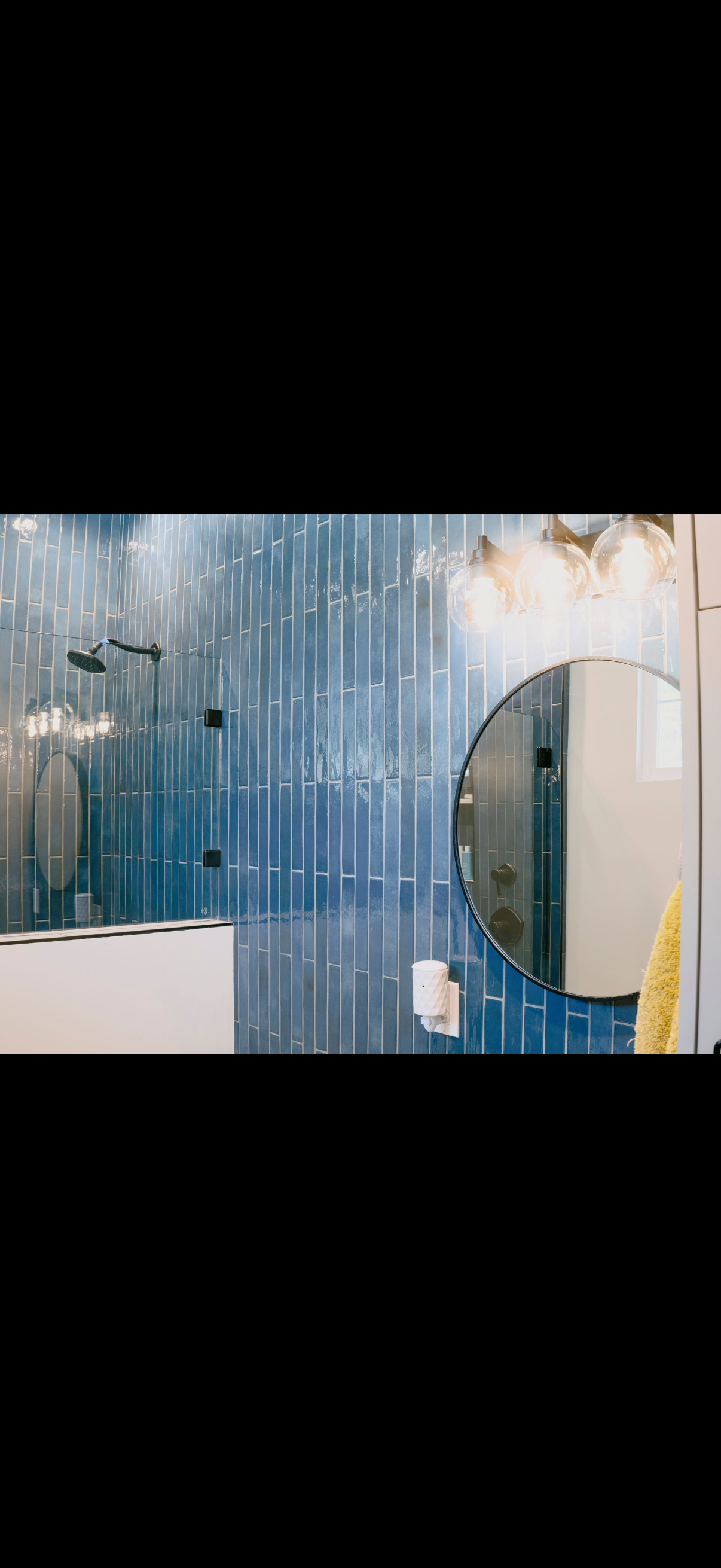 A blue-tiled bathroom with a round mirror. A white cabinet and a yellow towel are visible.