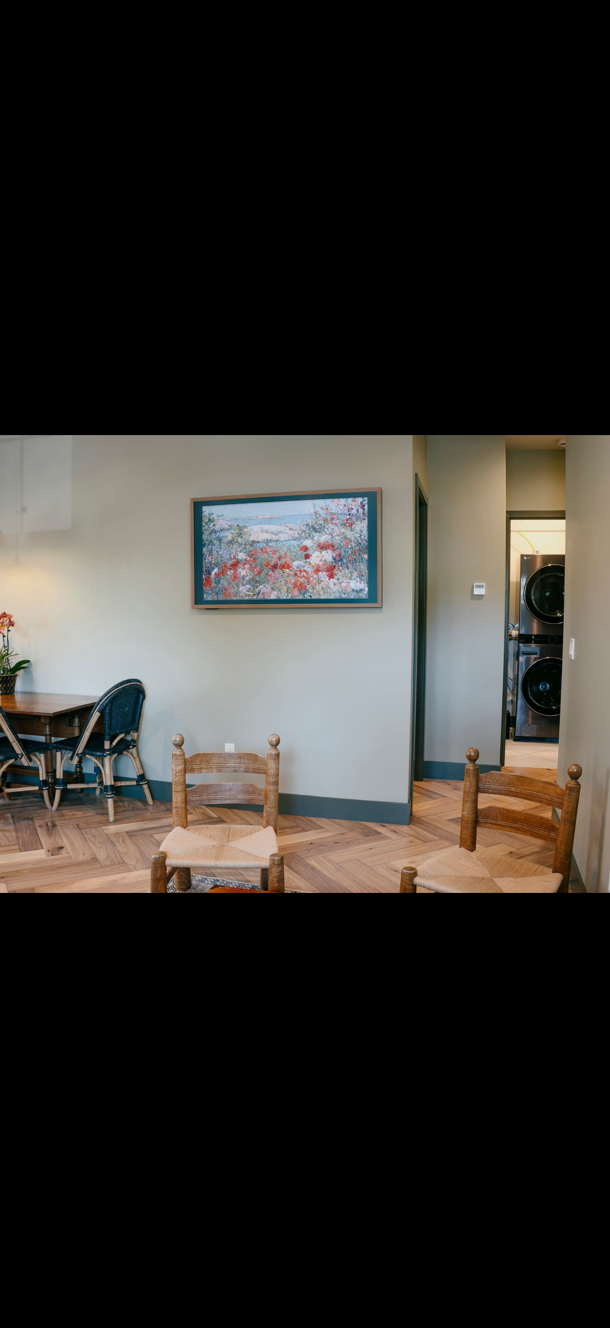 Room with chairs and a framed picture. Laundry room visible in the background.