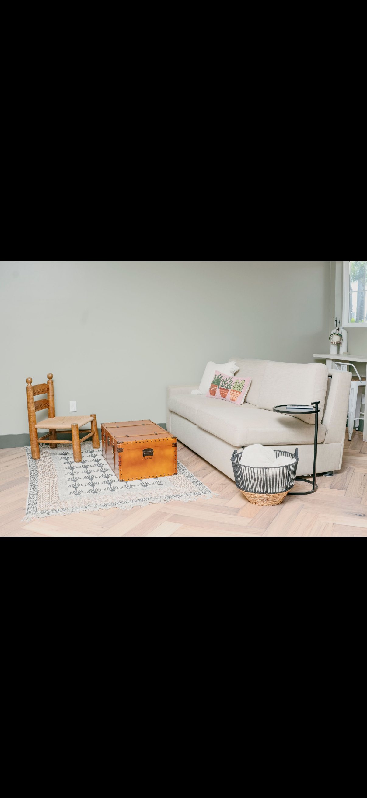 Living room with a white sofa, wooden chair, and trunk, a rug on light wood floors, and light green walls.