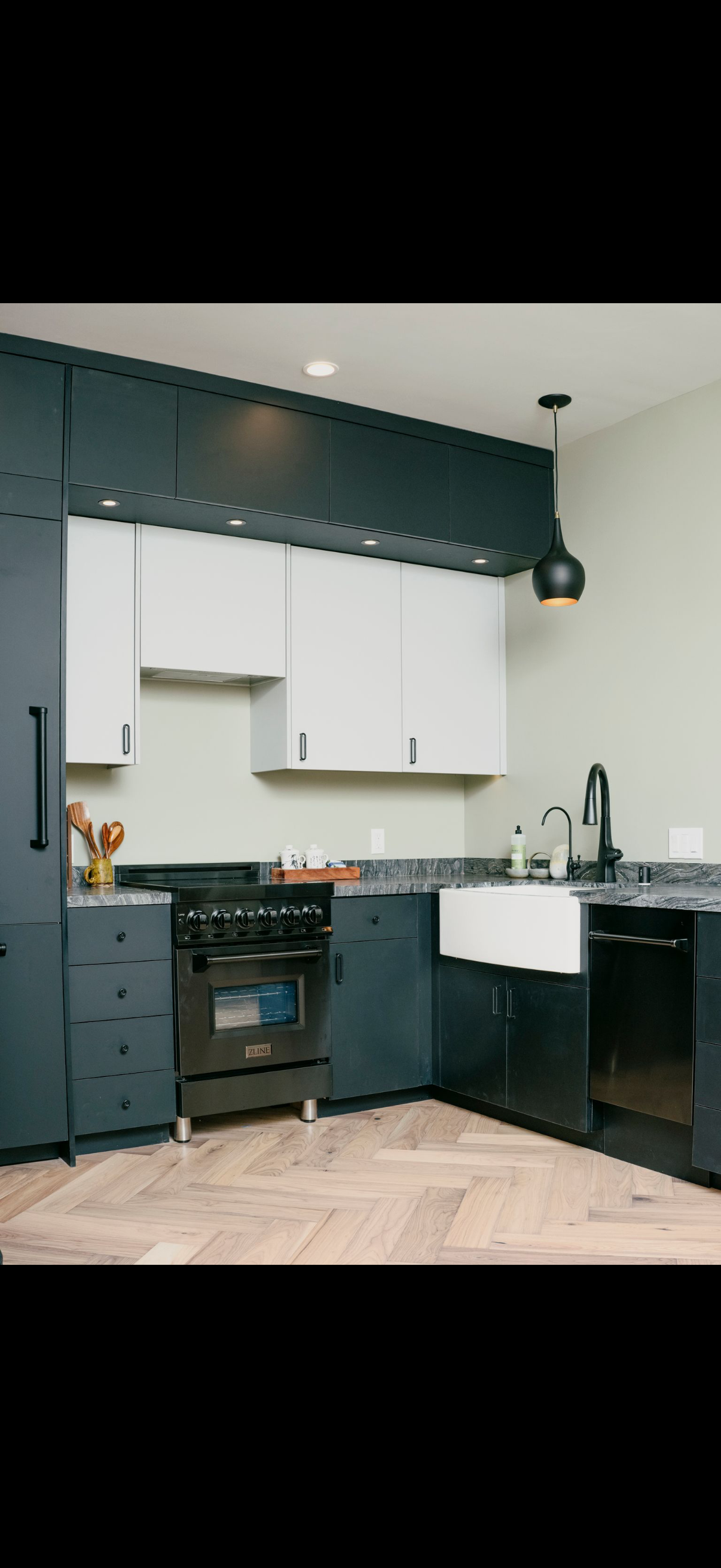 Modern kitchen with black and white cabinets, black range, white apron sink, and hardwood floor.