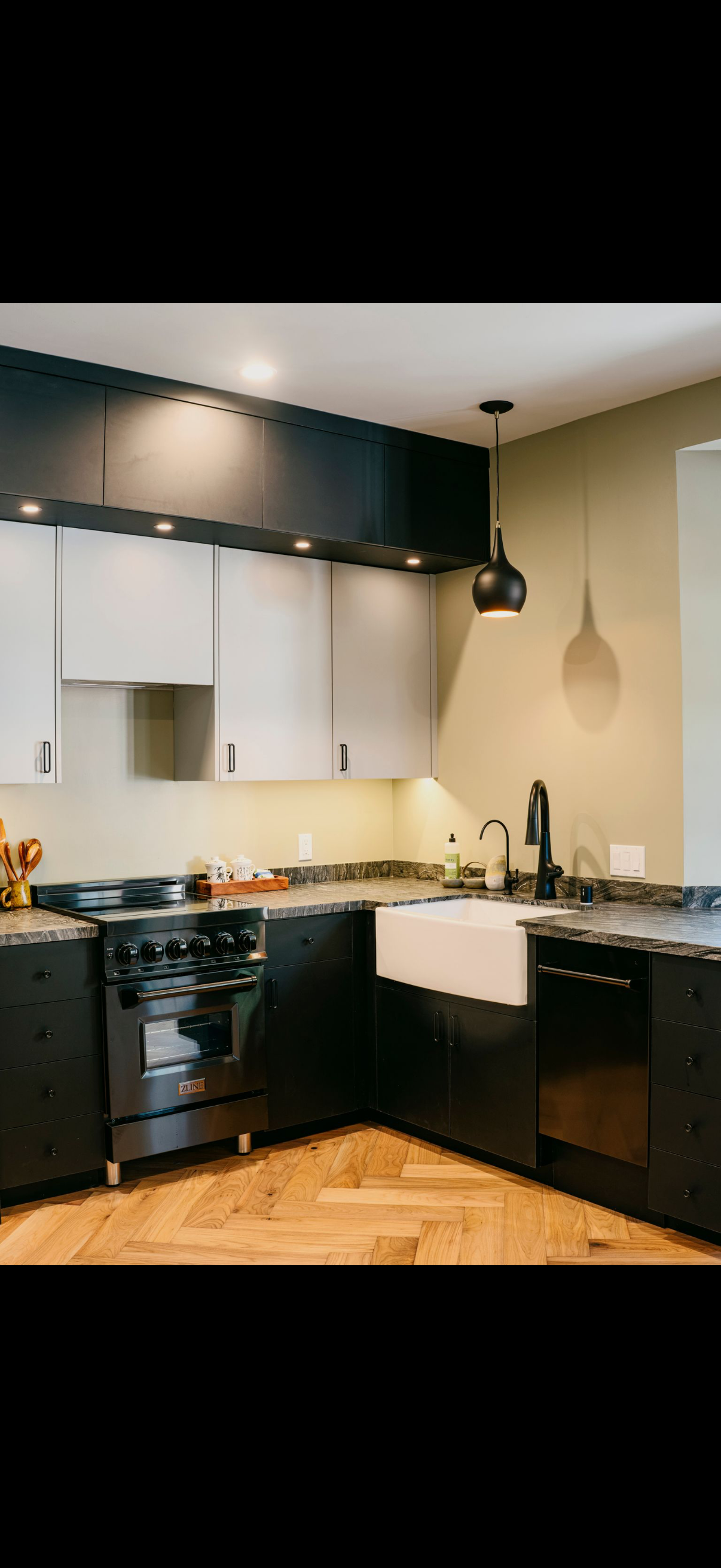A modern kitchen with black and white cabinetry, stainless steel appliances, and wood flooring.
