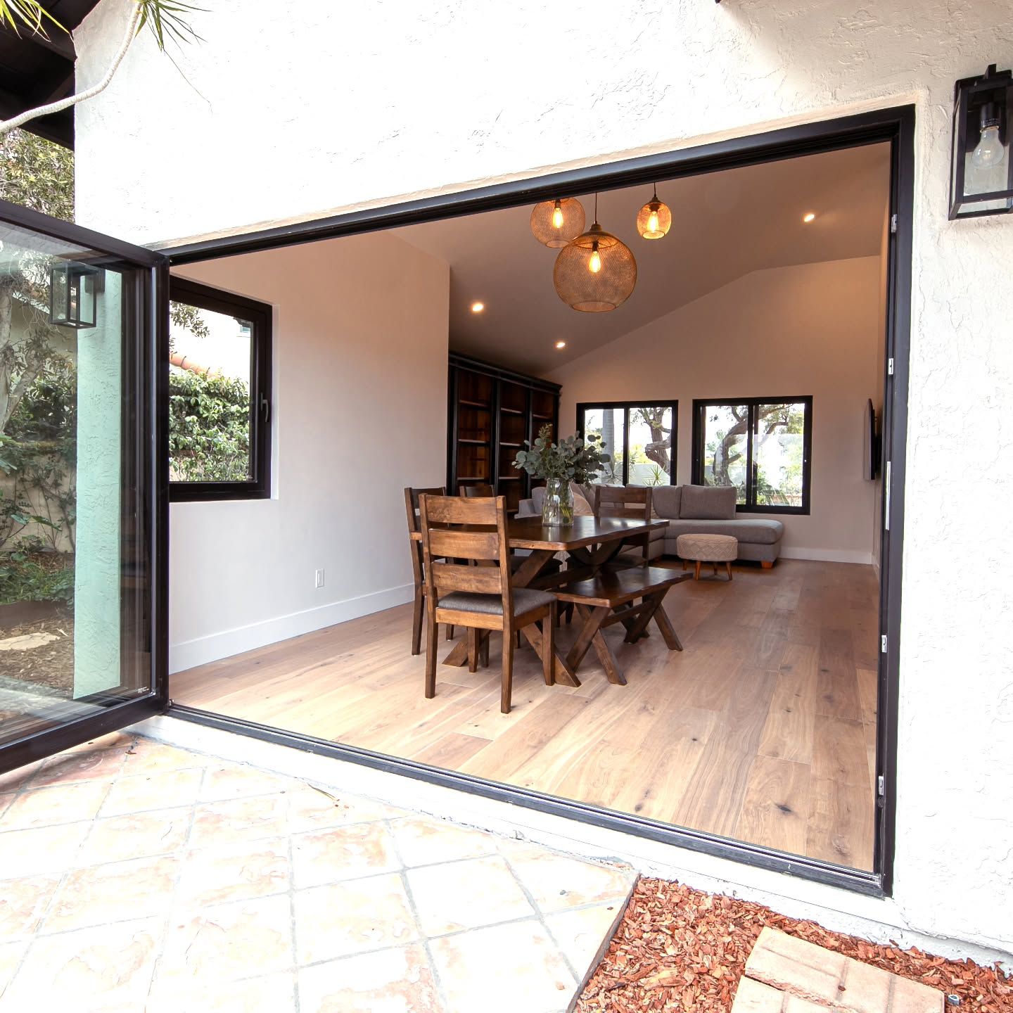 Open glass doors reveal a dining room with a wooden table, chairs, and a seating area.