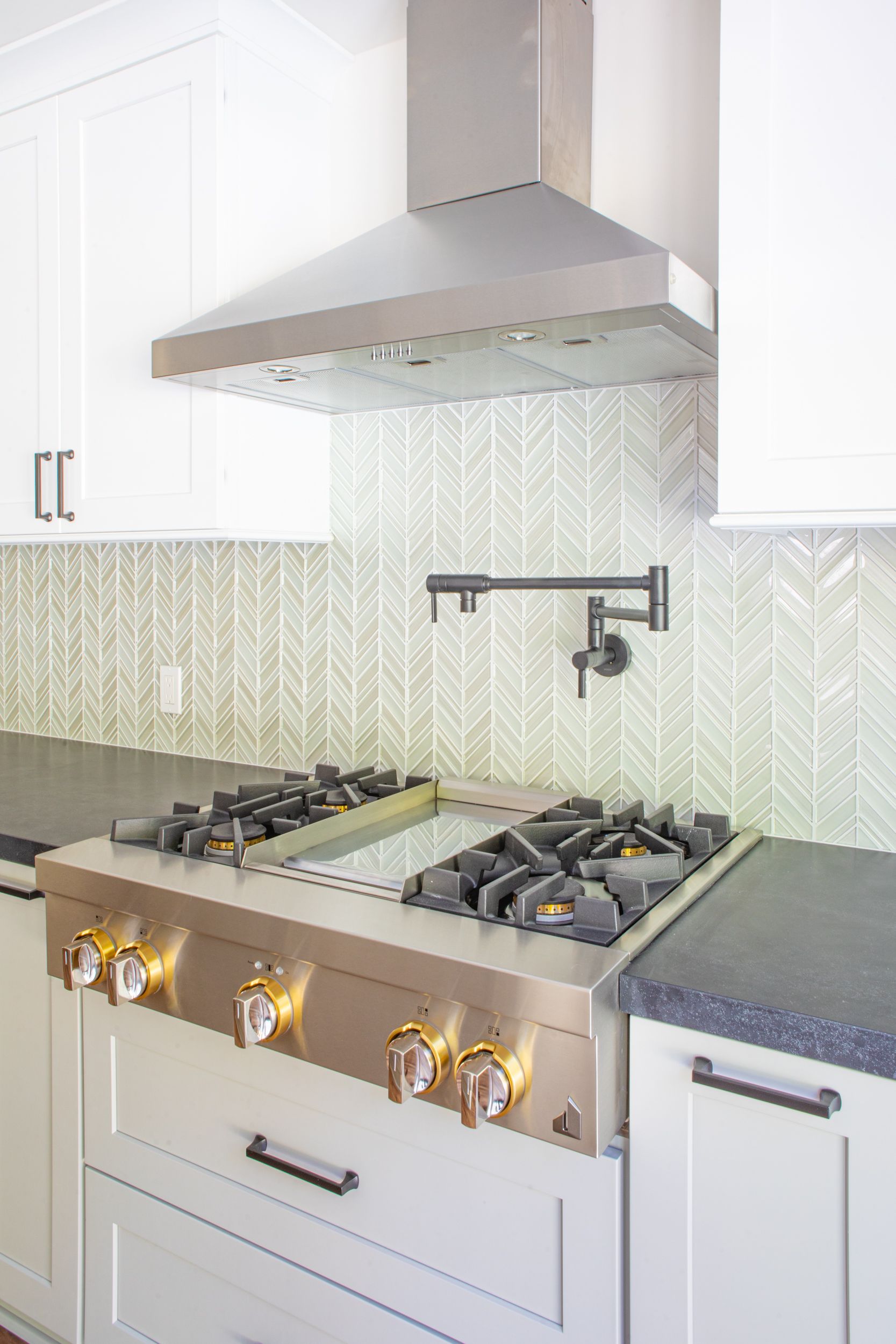 Stainless steel range with stovetop, range hood, and backsplash in modern kitchen.