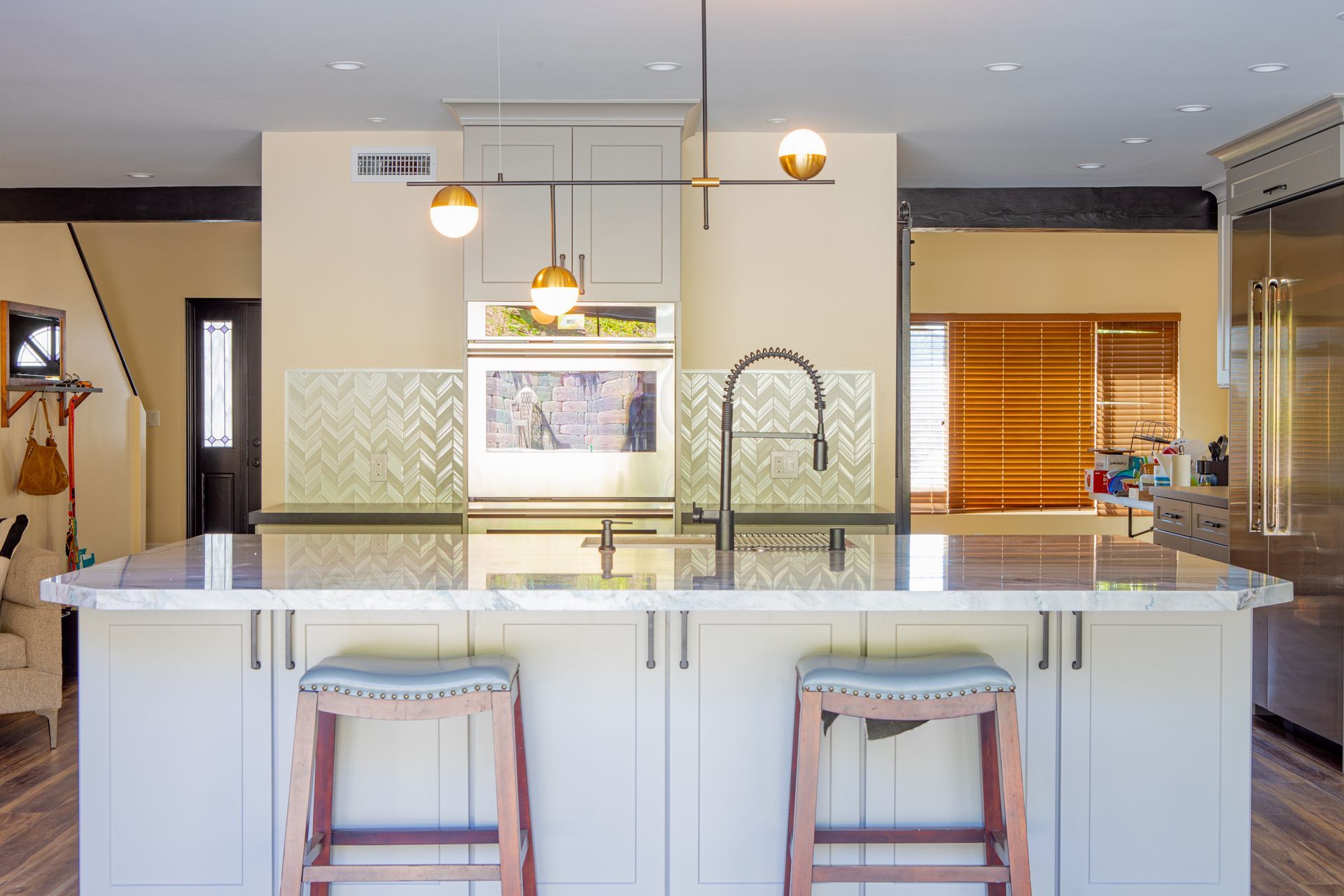 Modern kitchen with white island, two stools, gold pendant lights, and patterned backsplash.