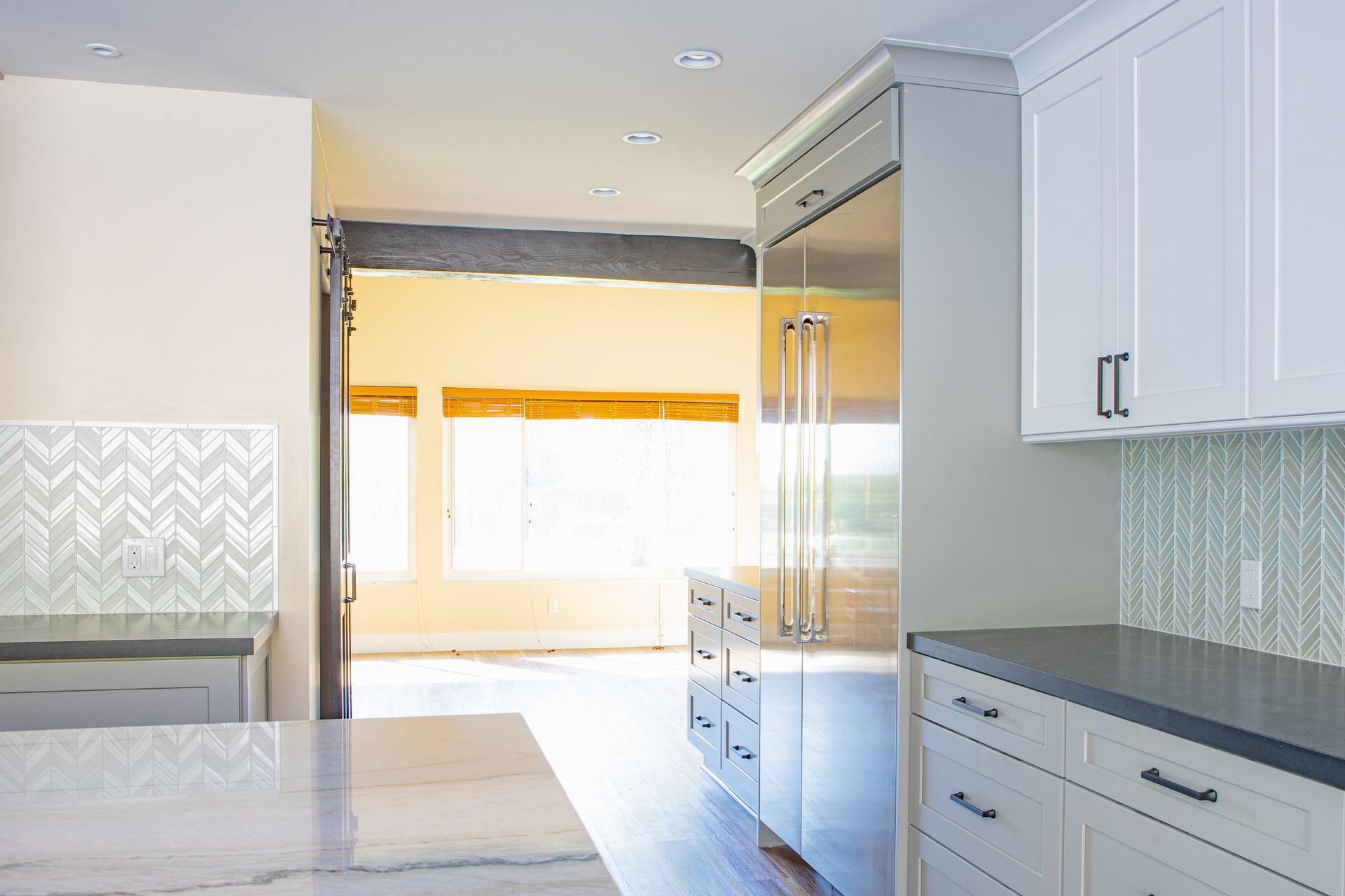 Kitchen with white cabinets, stainless steel fridge, and a bright doorway leading to the outside.