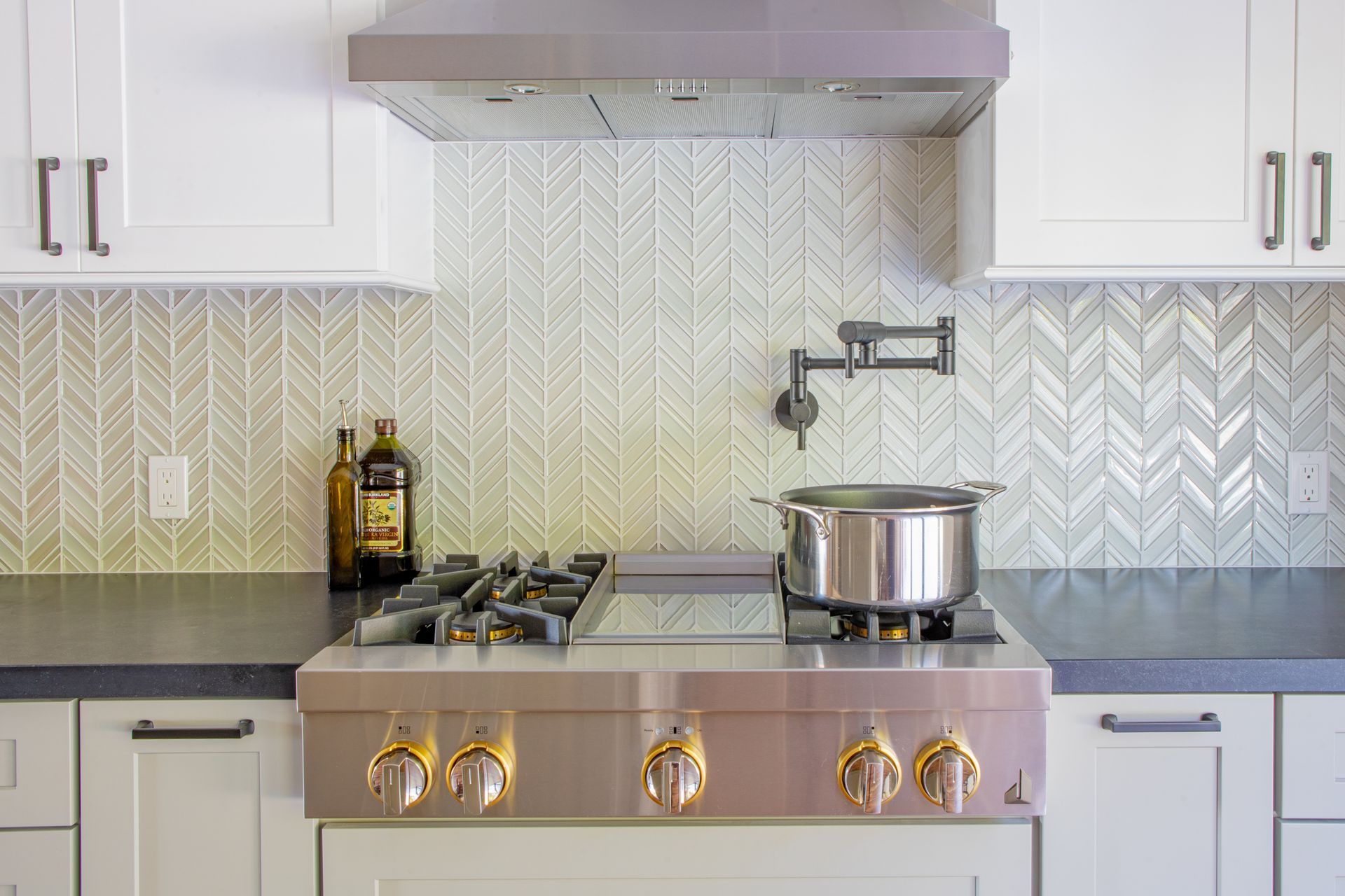 Modern kitchen with stainless steel range, pot on the stove, white cabinets, and patterned backsplash.