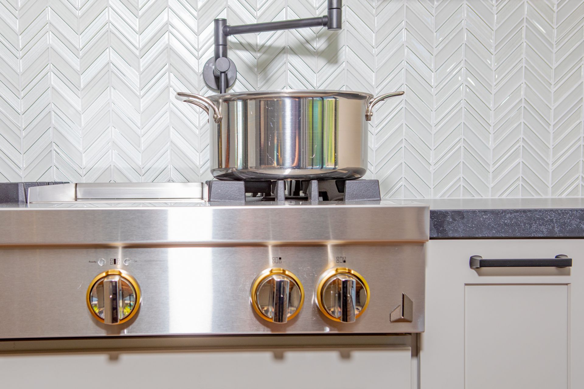 Stainless steel pot on a stove with decorative backsplash and an articulated pot filler.
