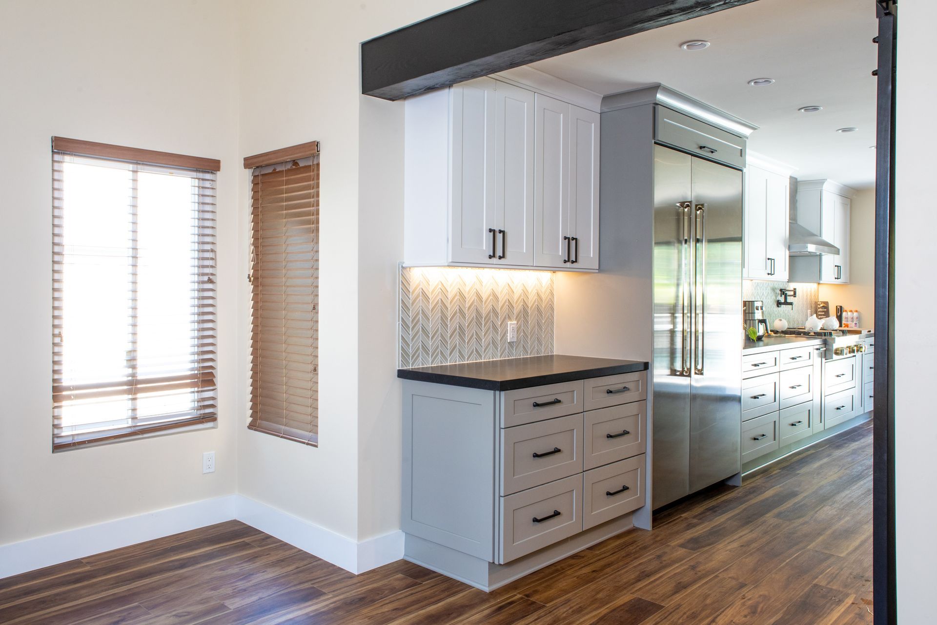 Kitchen with cabinets in white and gray, stainless steel refrigerator, and wood floors.