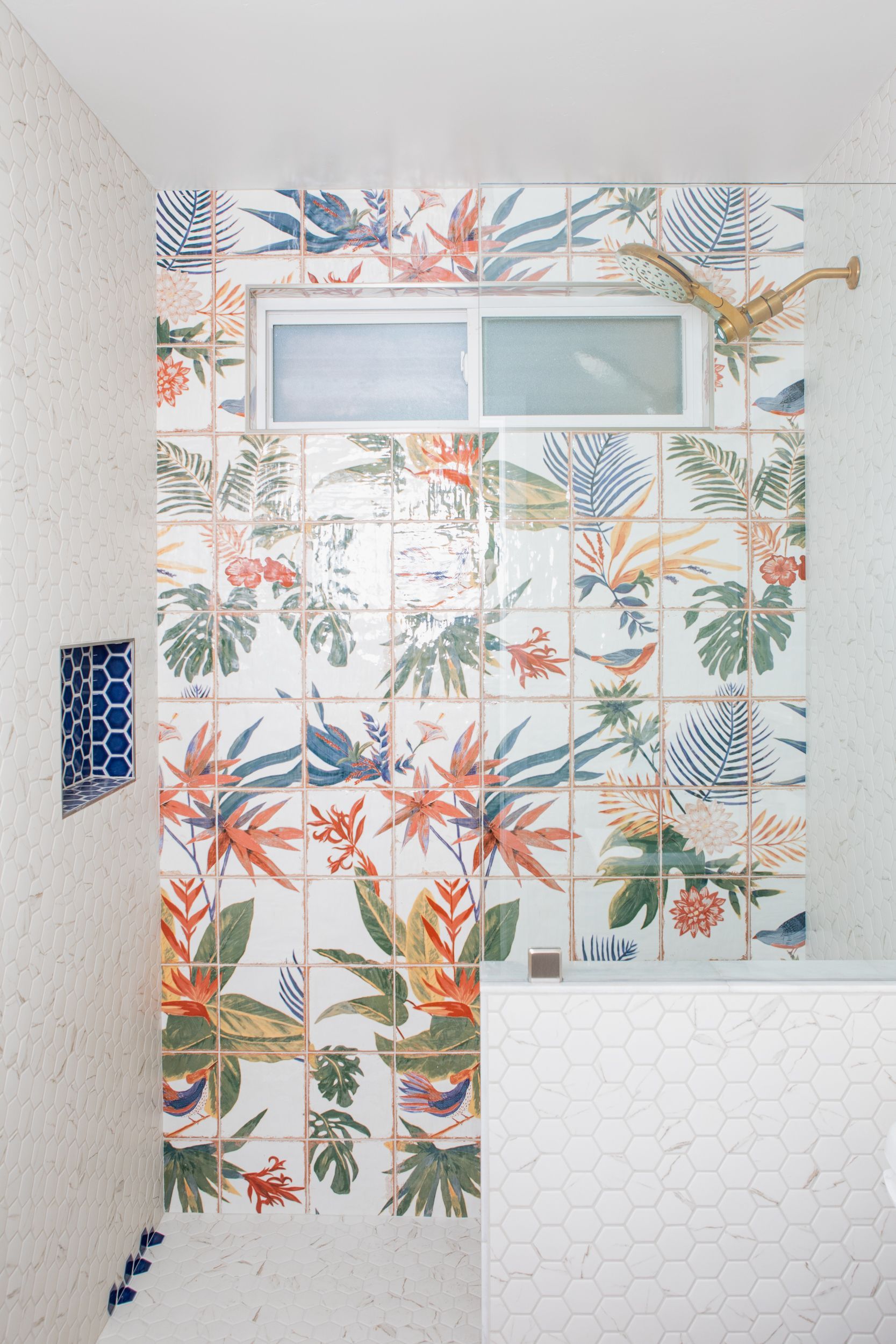 Shower with floral patterned tiles, small window, and white pebble tile walls.