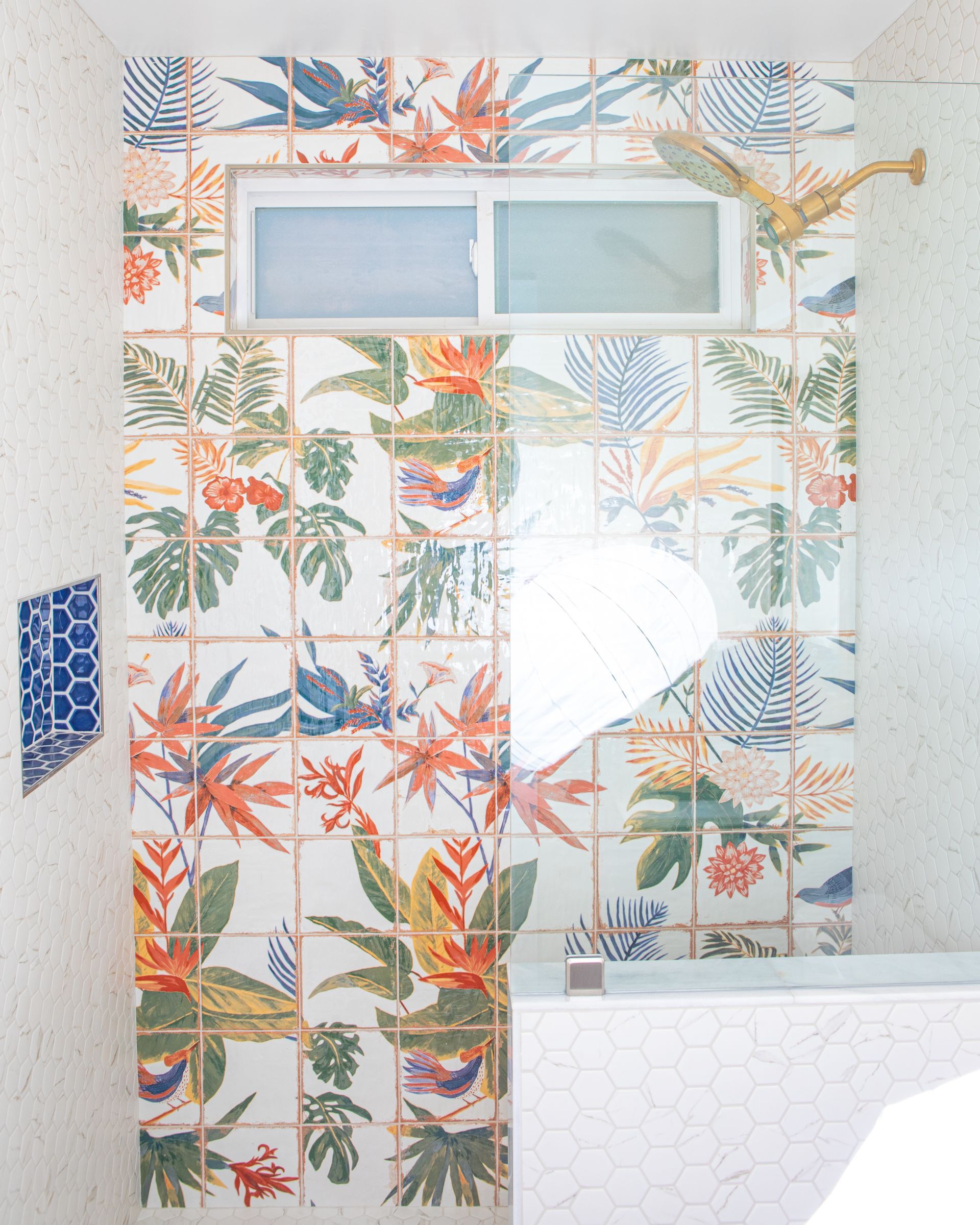 Bathroom with floral tiles, window, and gold showerhead.