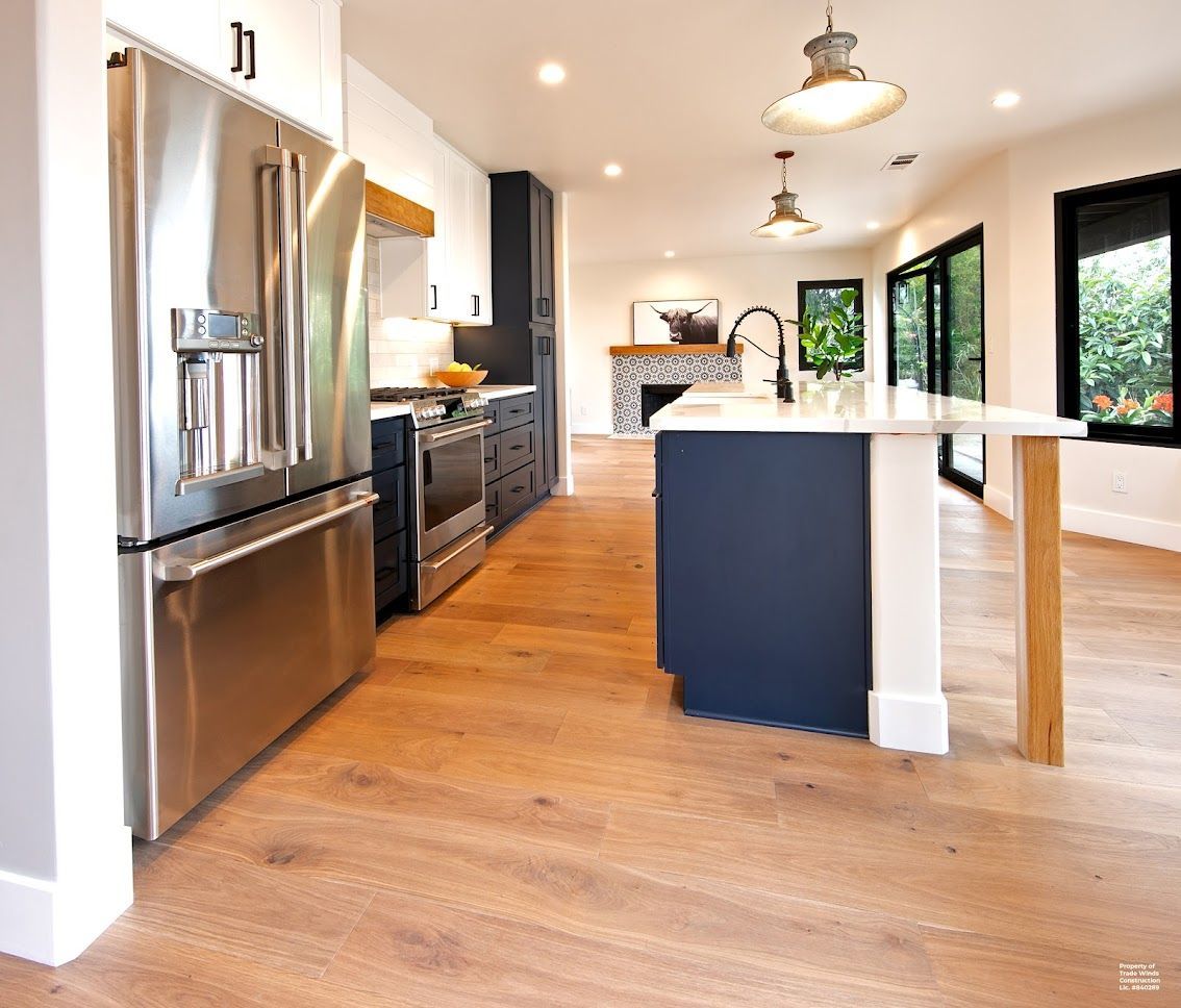 Modern kitchen with stainless steel appliances, blue island, hardwood floors, and black-framed windows.