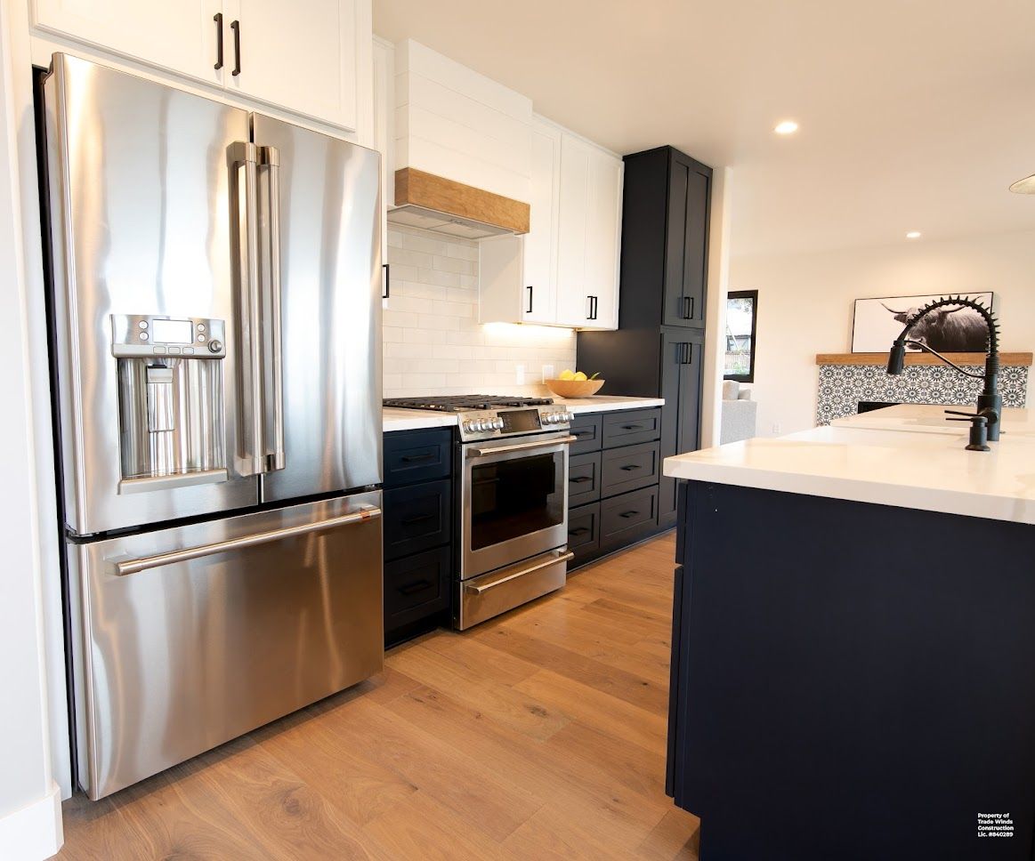Modern kitchen with stainless steel appliances, navy cabinets, and wooden flooring.