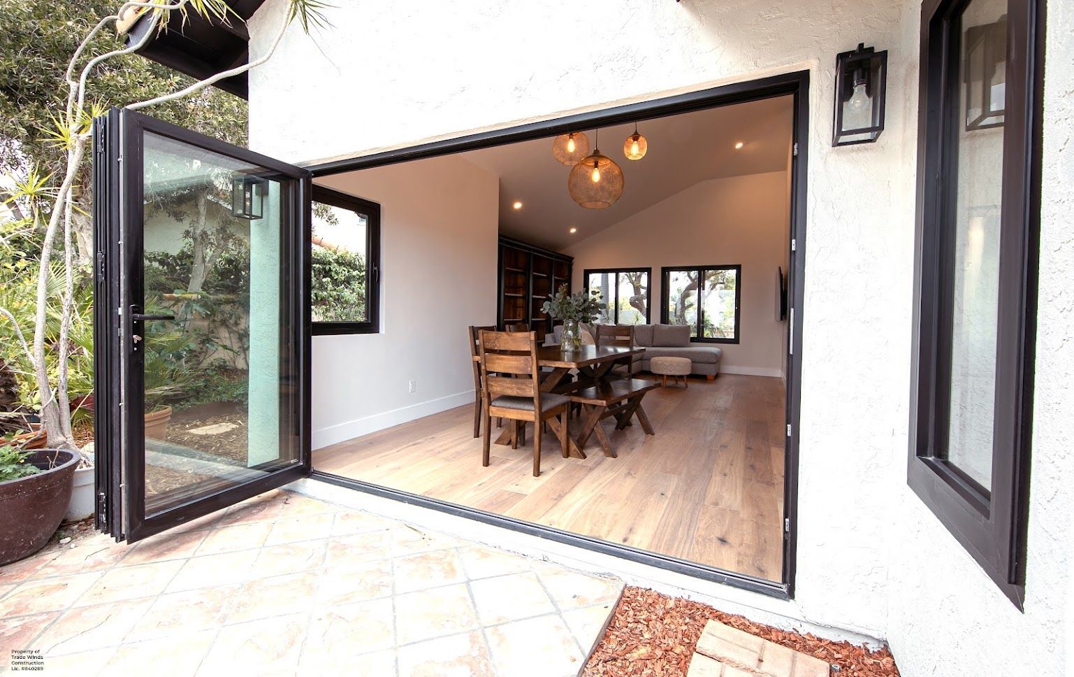Open folding glass doors reveal a dining room with wooden table and chairs.