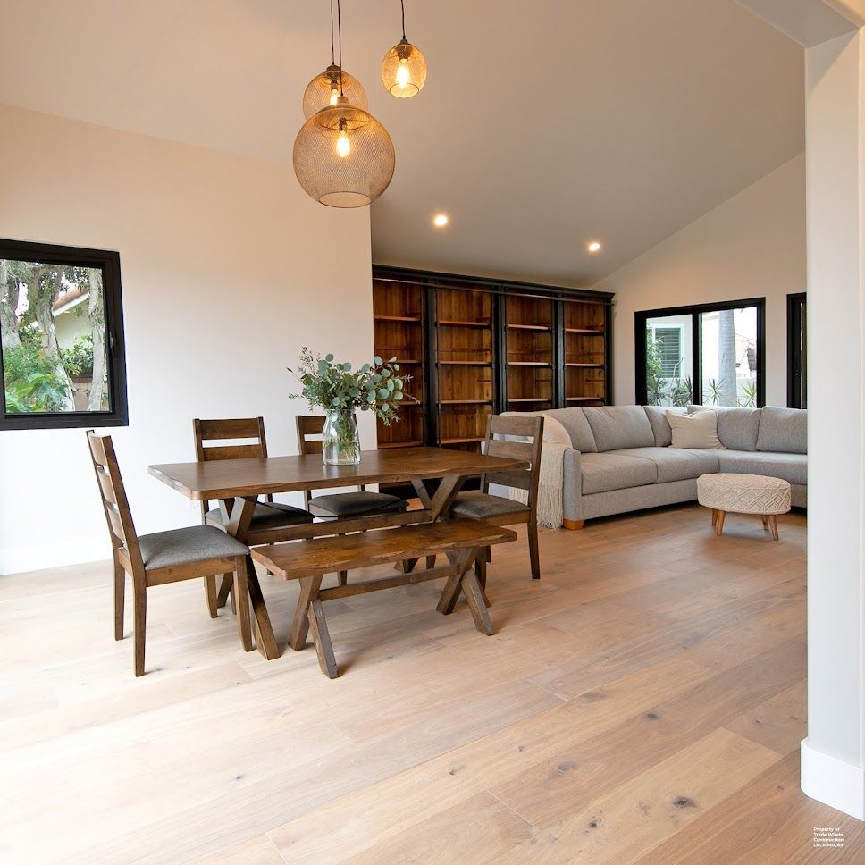 Dining room with wooden table, bench, and chairs, open to a living room with a sectional sofa and bookshelves.