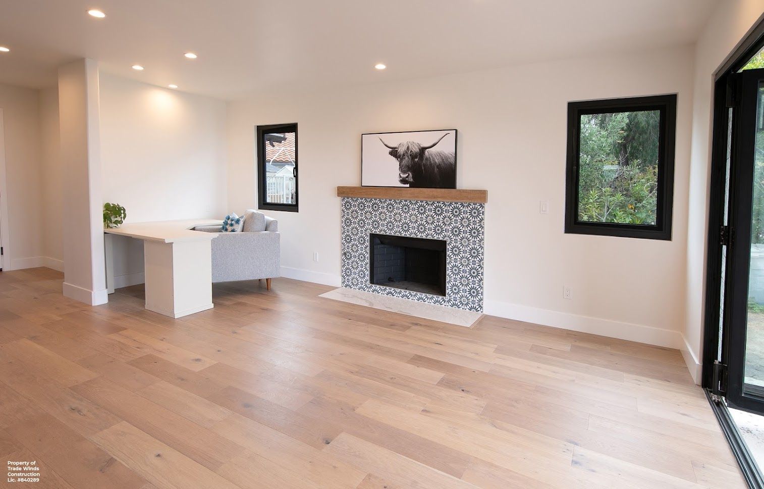 Spacious, bright living room with fireplace, hardwood floors, white walls, and large windows.