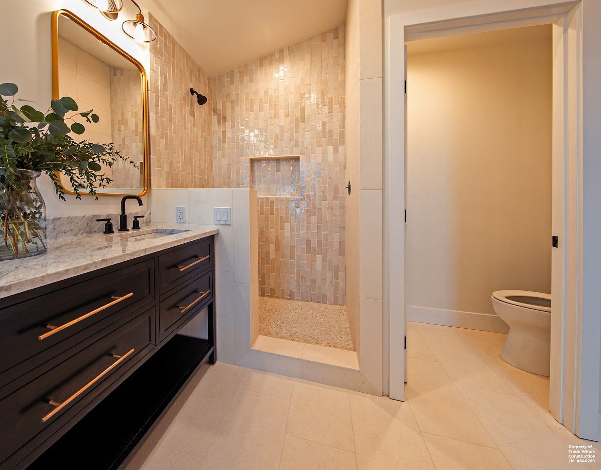 Bathroom with dark vanity, gold-framed mirror, tiled shower, and open door to a toilet.