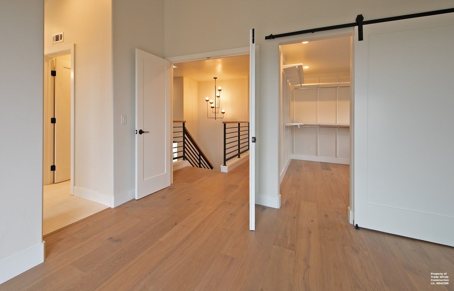 Bright hallway with light wood floor, white walls, and open doors to rooms, stairs, and a pantry.