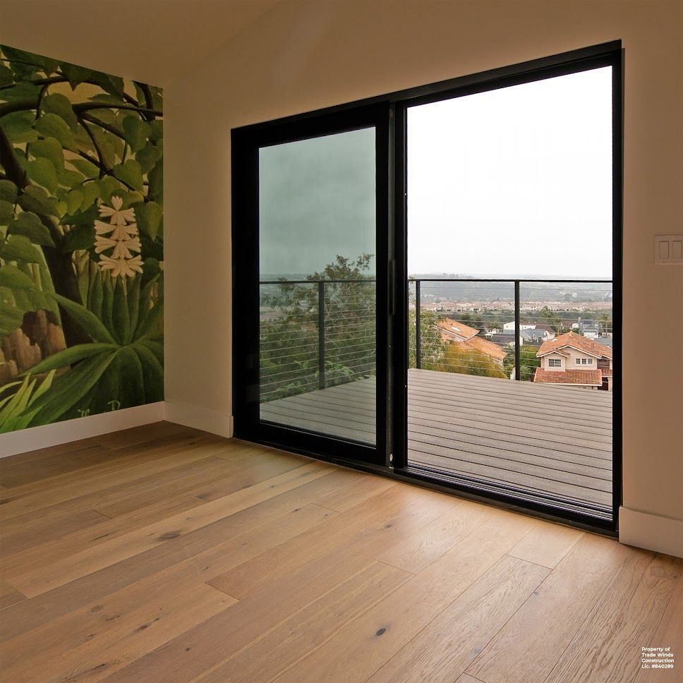 Wooden floor, black-framed glass door to a balcony overlooking a cityscape; a mural on the wall.