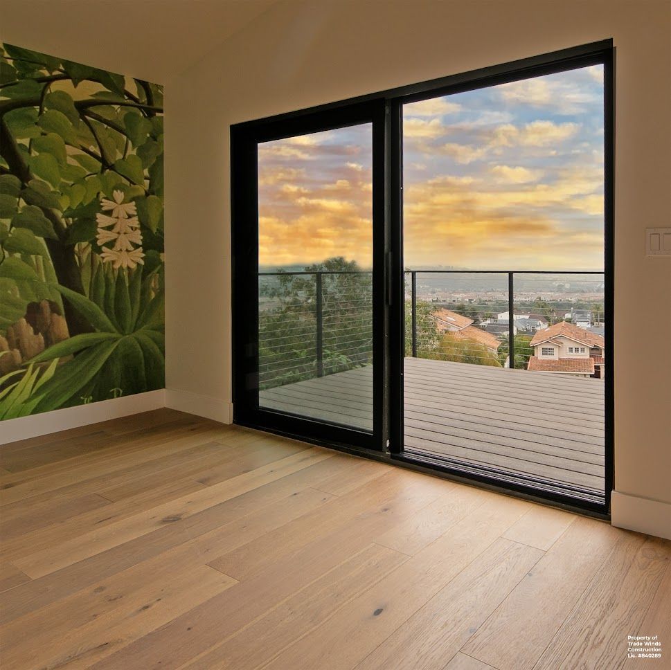 Room with hardwood floor, large window overlooking cityscape and sunset. Mural on the wall.