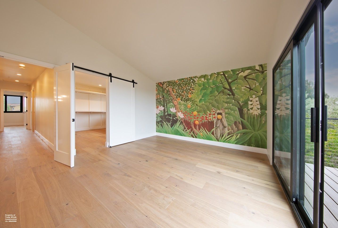 Empty room with wood floors, large sliding glass door, a jungle mural, and a sliding white door.