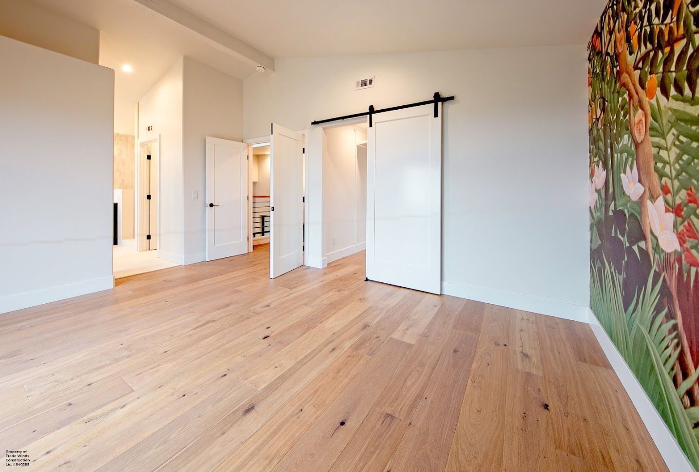 Light-filled bedroom with wooden floors, white walls, and open doors. Large artwork on the right.