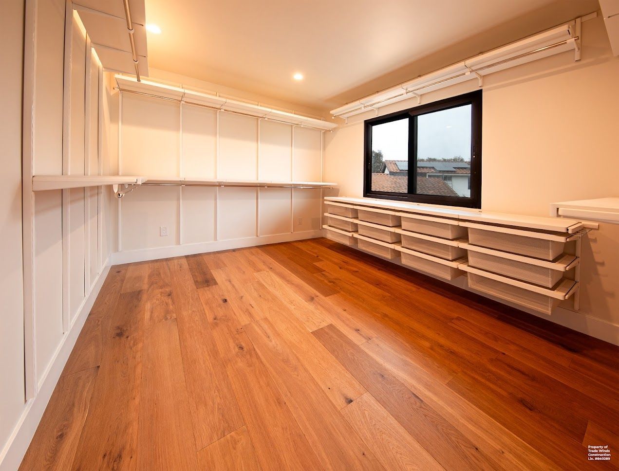 Empty walk-in closet with white shelving, hardwood floor, and a dark window.