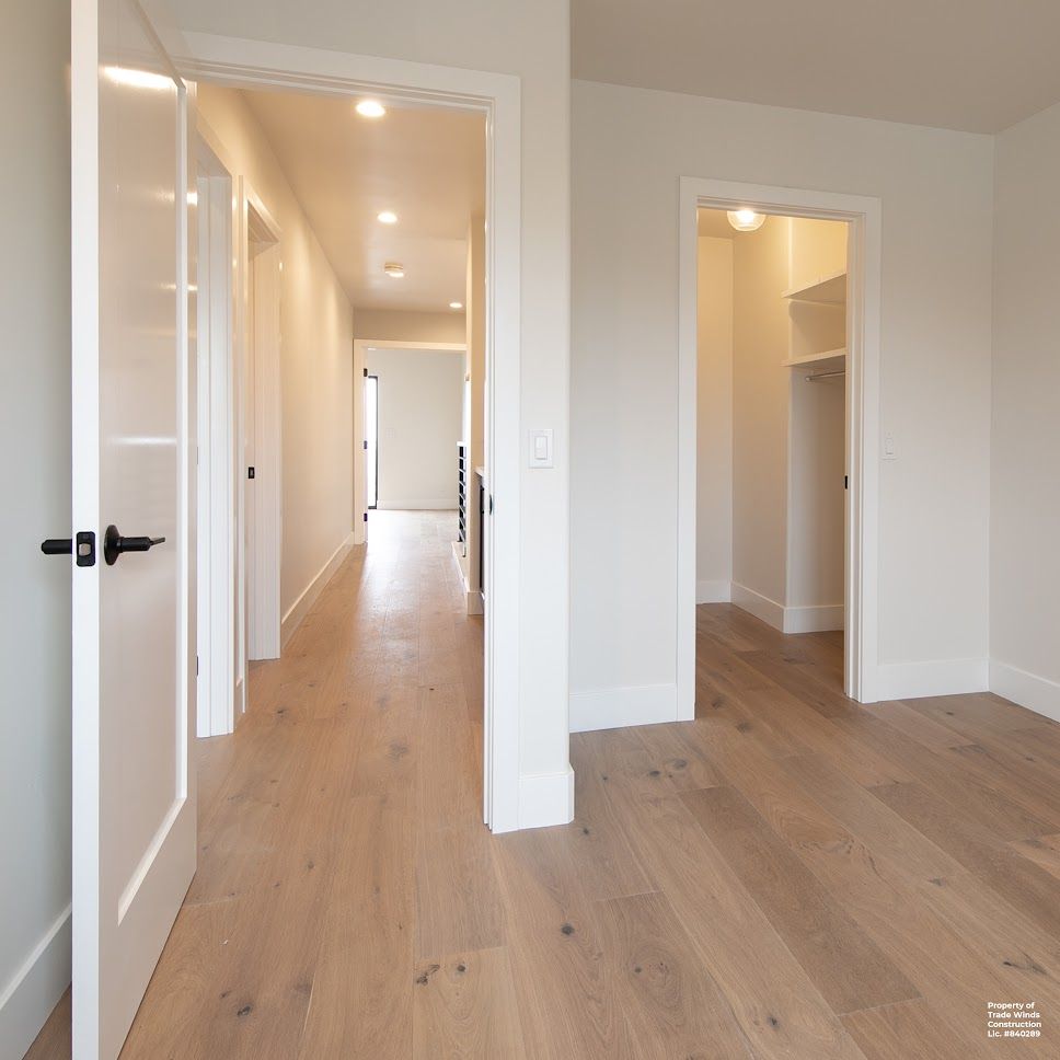 Hallway with light wood floors and white walls. Open doors lead to more rooms.