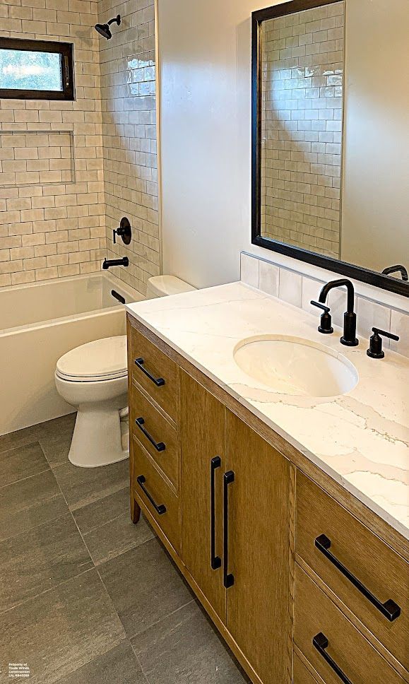 Bathroom with light wood vanity, marble countertop, black fixtures, and tiled shower.