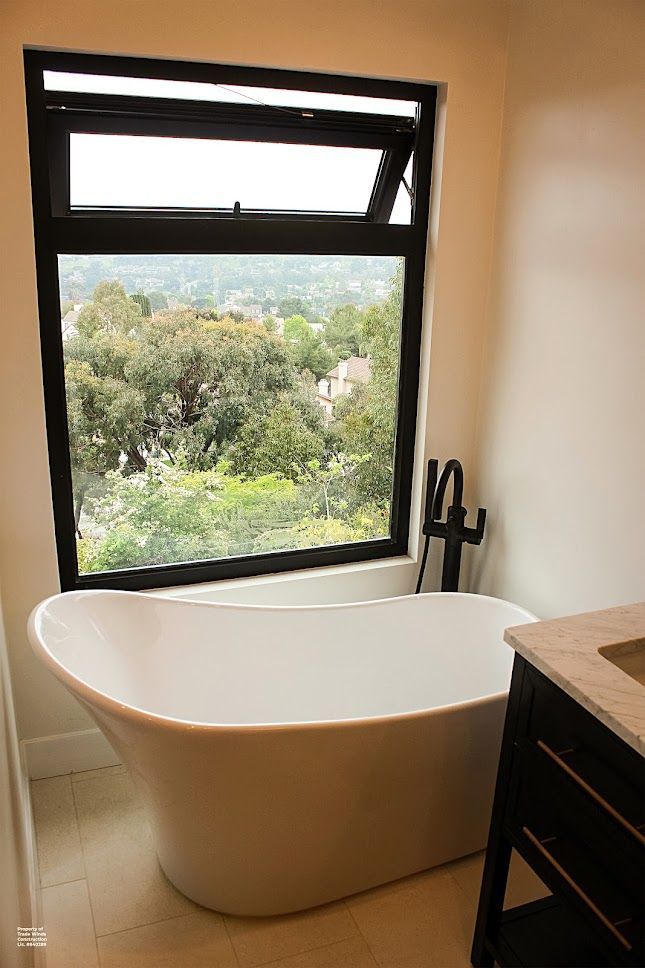 Freestanding white tub by a window with a view. Black-framed window is open.