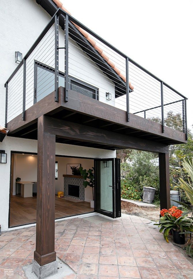 Two-story house with a deck. Dark brown deck supports, black railing, and a terracotta patio.