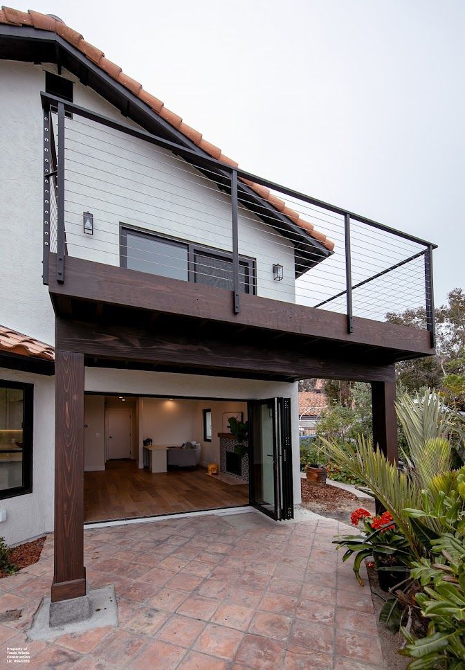 Two-story house with a deck. Exterior shot with brown columns, black railing, and open doors to the interior.