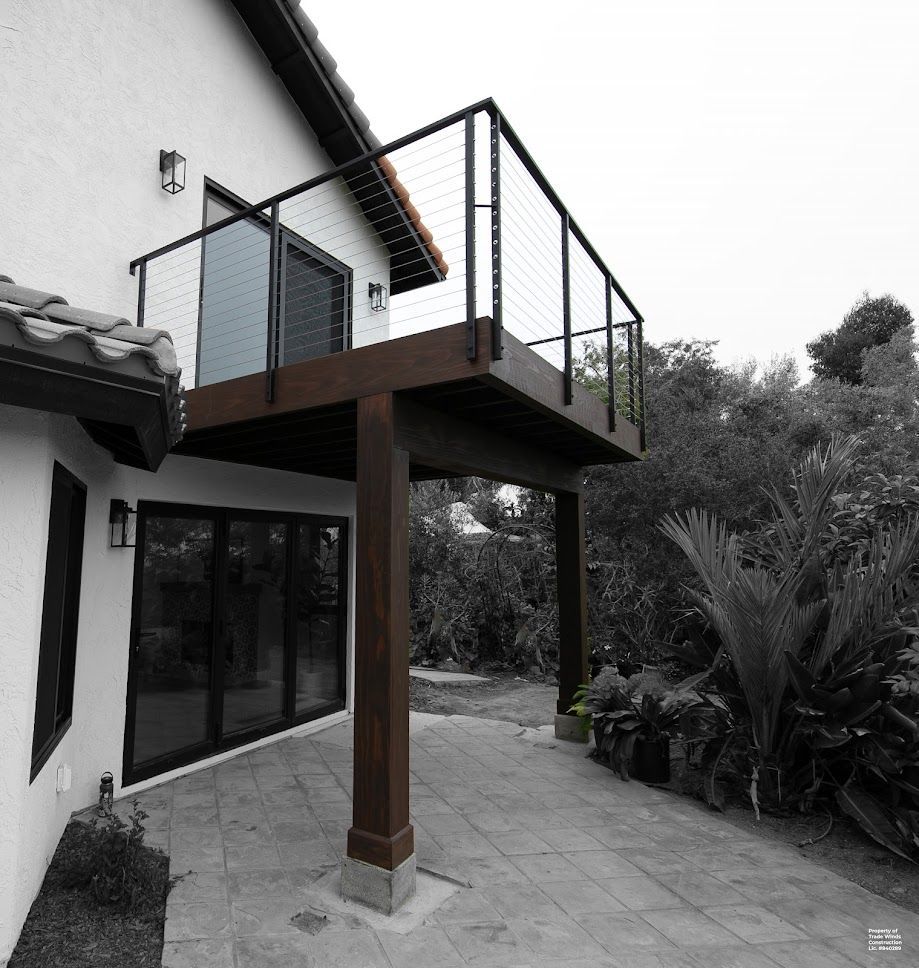 Deck with black railing and glass panels, supported by a wooden post, overlooking a patio.