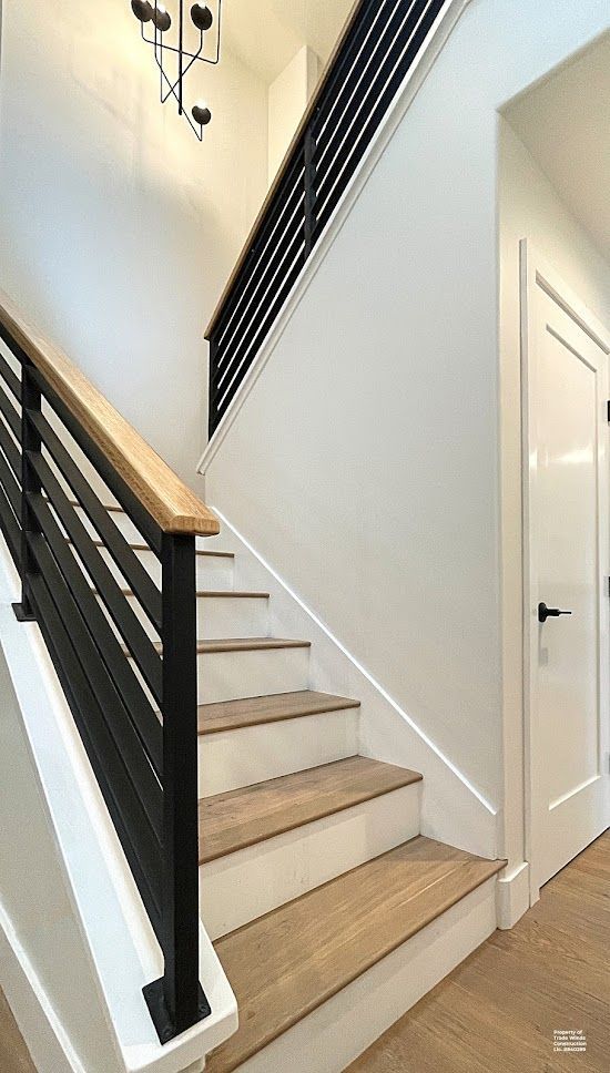 Staircase with light wood steps, black railing, white walls, and a black door handle.
