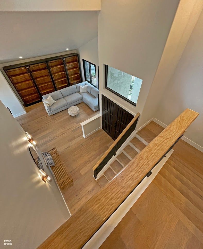 High-angle view of a two-story living area with a staircase, light wood floors, and a gray sectional sofa.