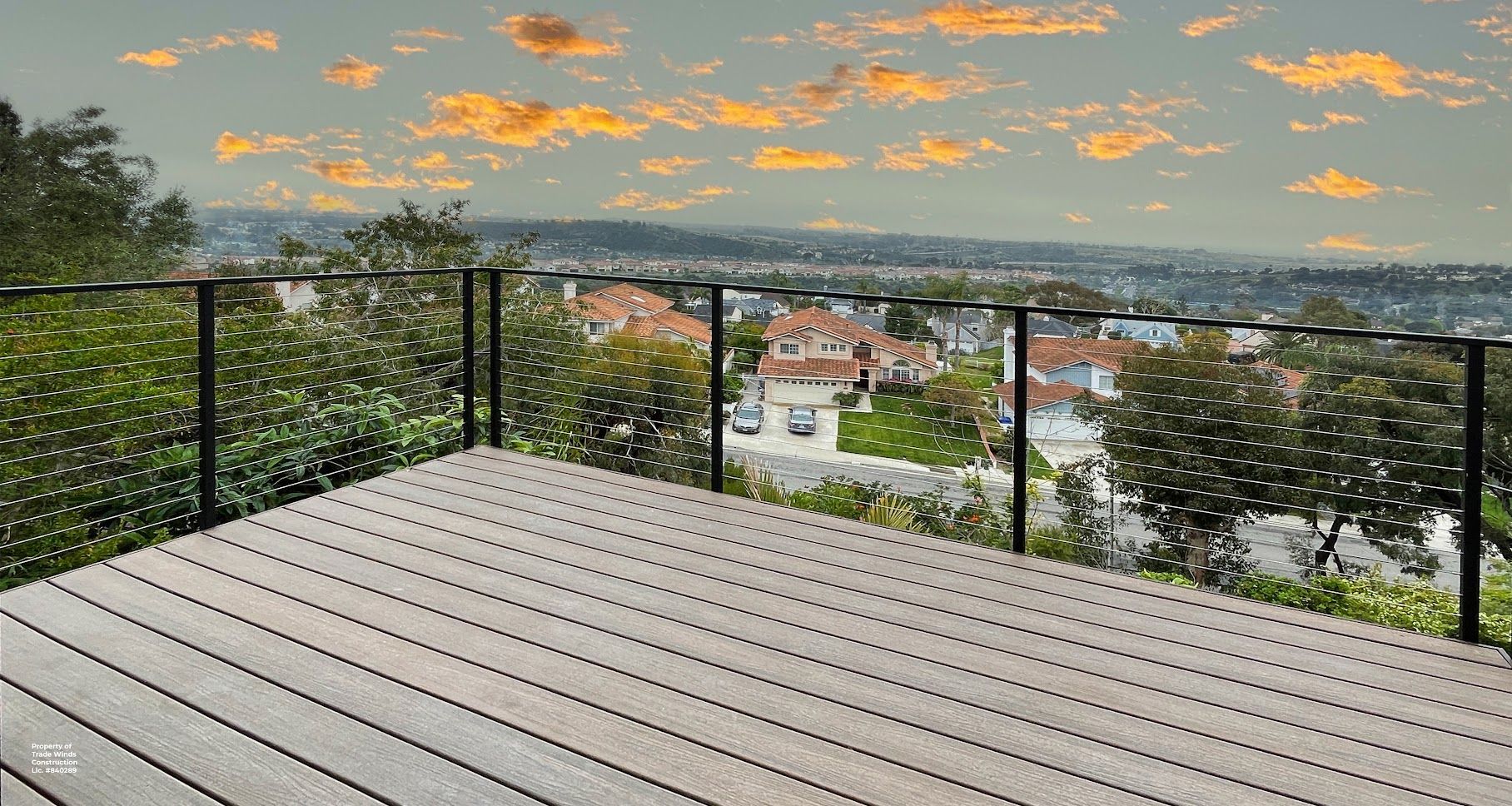 Wooden deck overlooking a suburban neighborhood at sunset, with black railing and string lights.