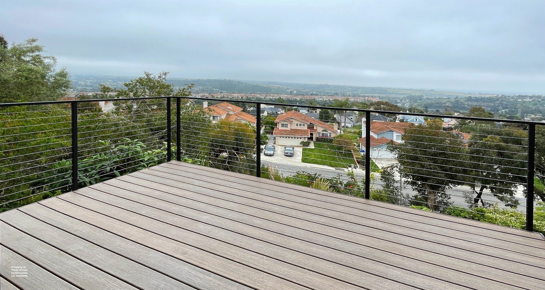 Wooden deck with black railing overlooking a residential neighborhood on a cloudy day.
