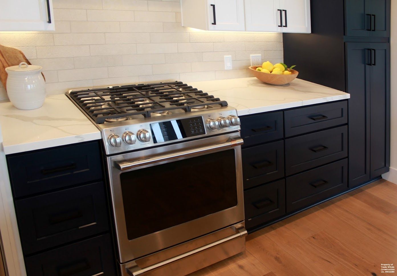 Modern kitchen with black cabinets, stainless steel stove, white countertops, and wood floors.