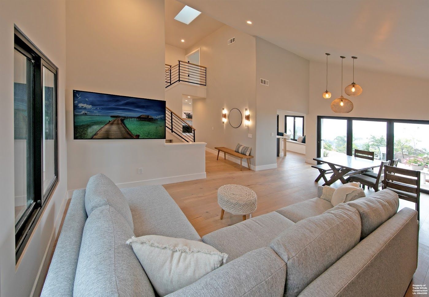 Modern, open-concept living room with light wood floors, sectional sofa, dining area, and large windows.