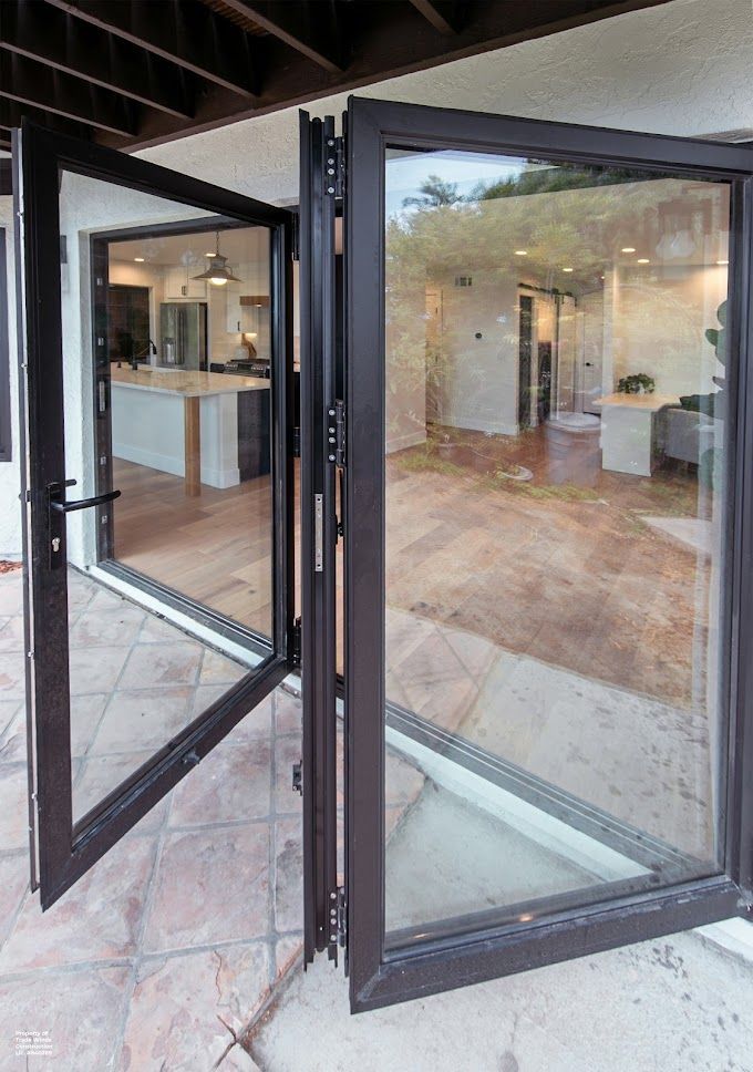 Folding glass doors, bronze frames, open onto a patio, revealing a kitchen and interior.
