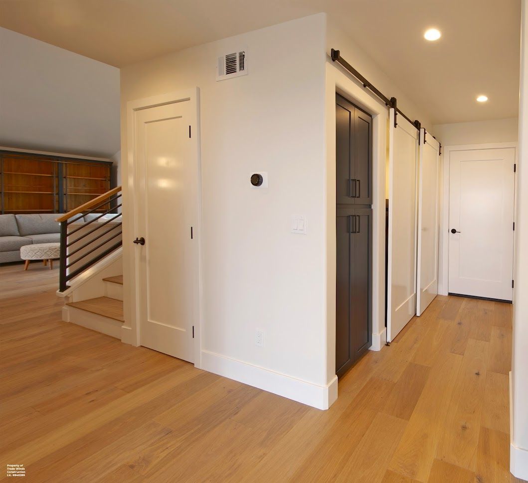 Hallway with hardwood floors, white walls, doors, and a staircase.