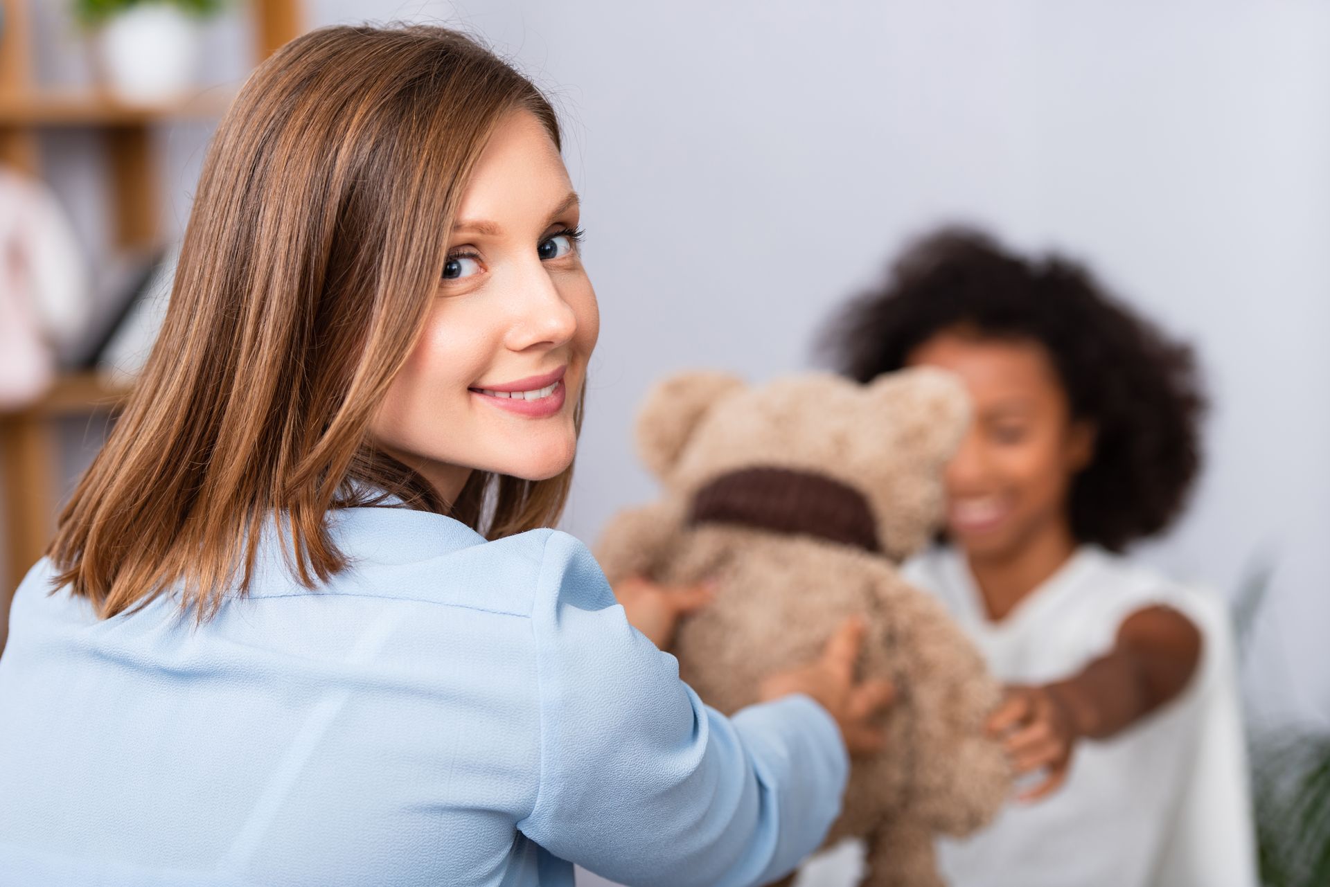 A woman holding a teddy bear in front of a little girl