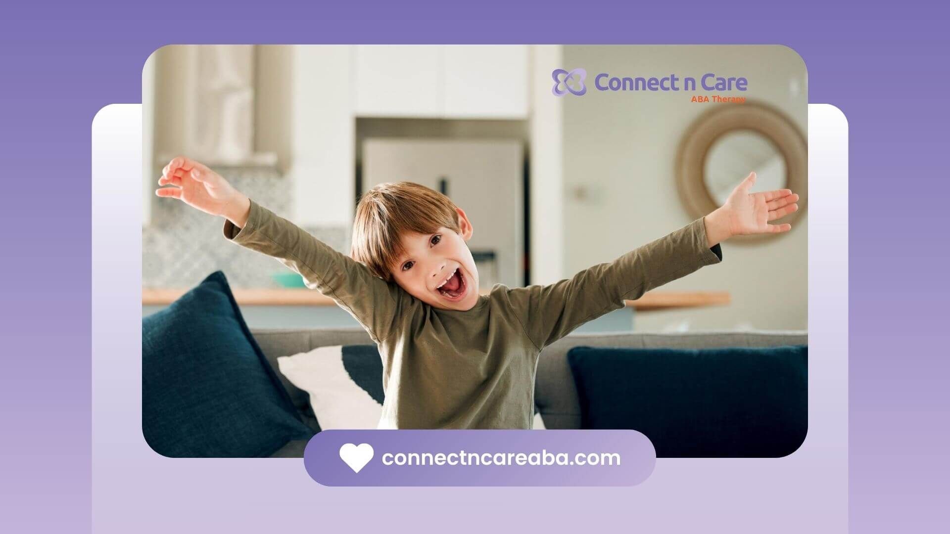 A smiling young boy with autism raises his arms on a couch.