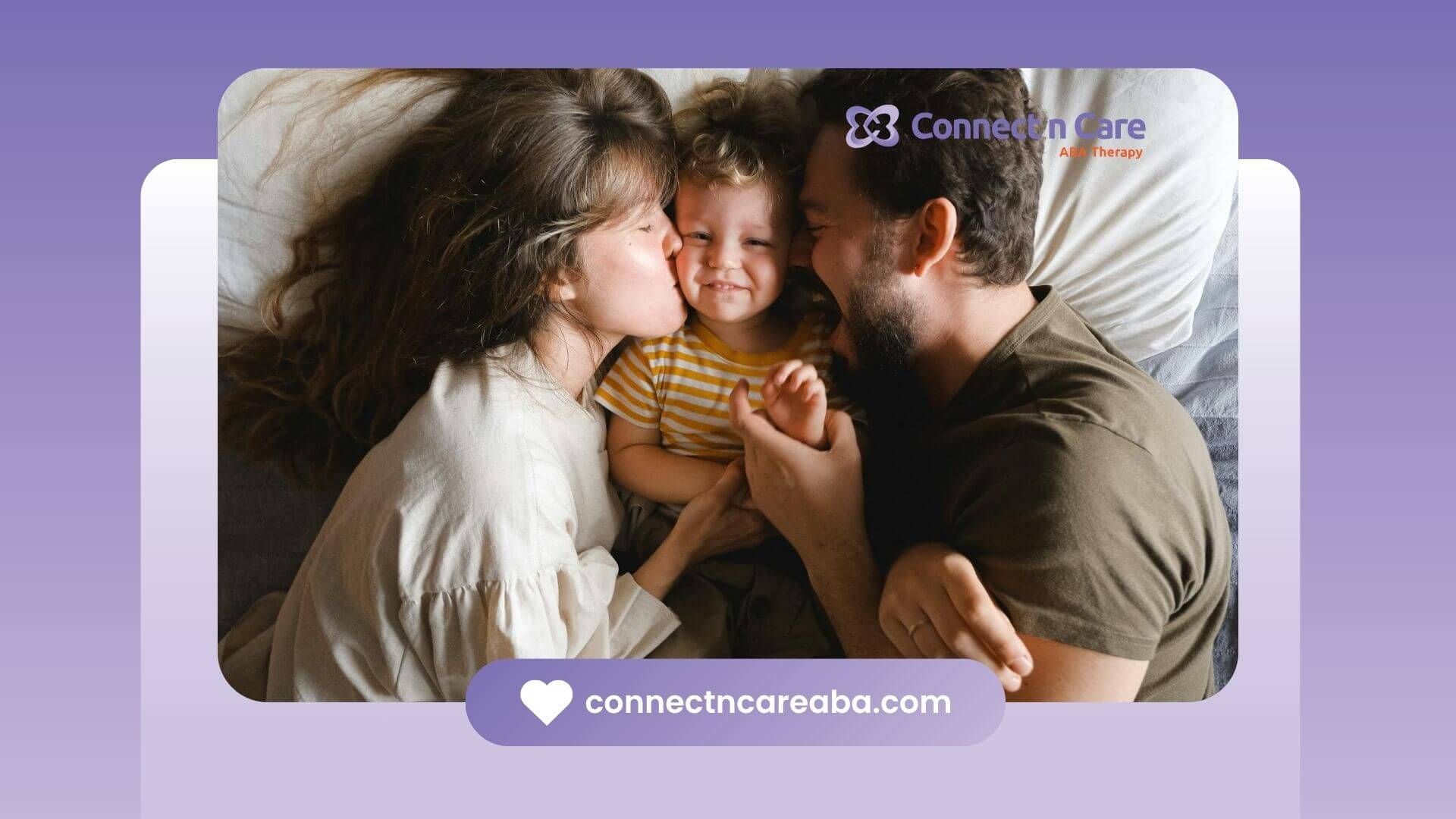 Smiling autistic child gets kissed by ABA parents as they lie close together on a cozy bed.