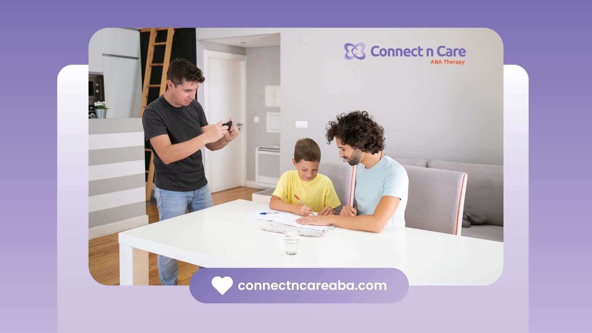 Man taking a photo of his son coloring on a piece of paper, sitting at a table with a glass of water